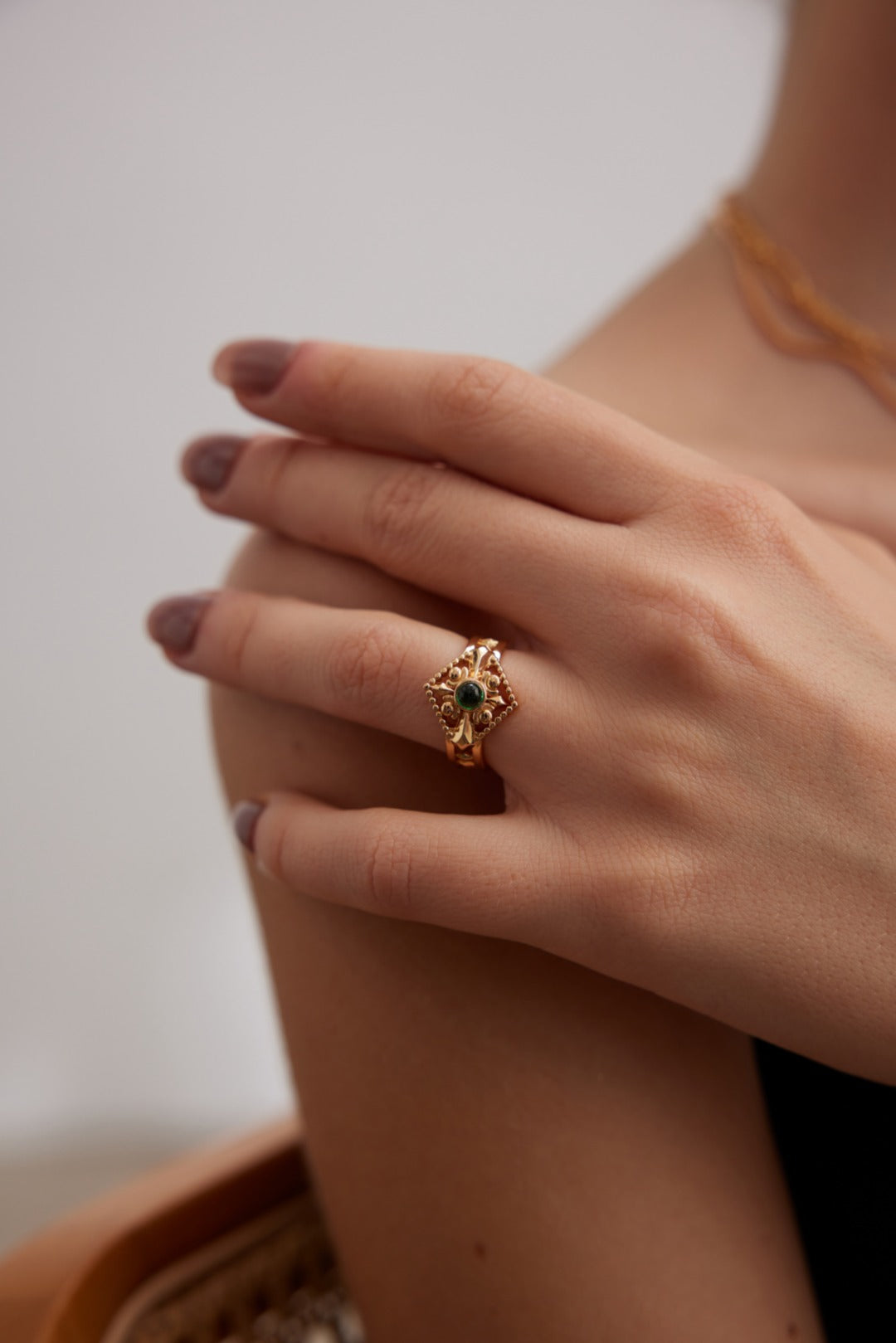 Close-up of a hand wearing a gold ring with a green gemstone on a neutral background