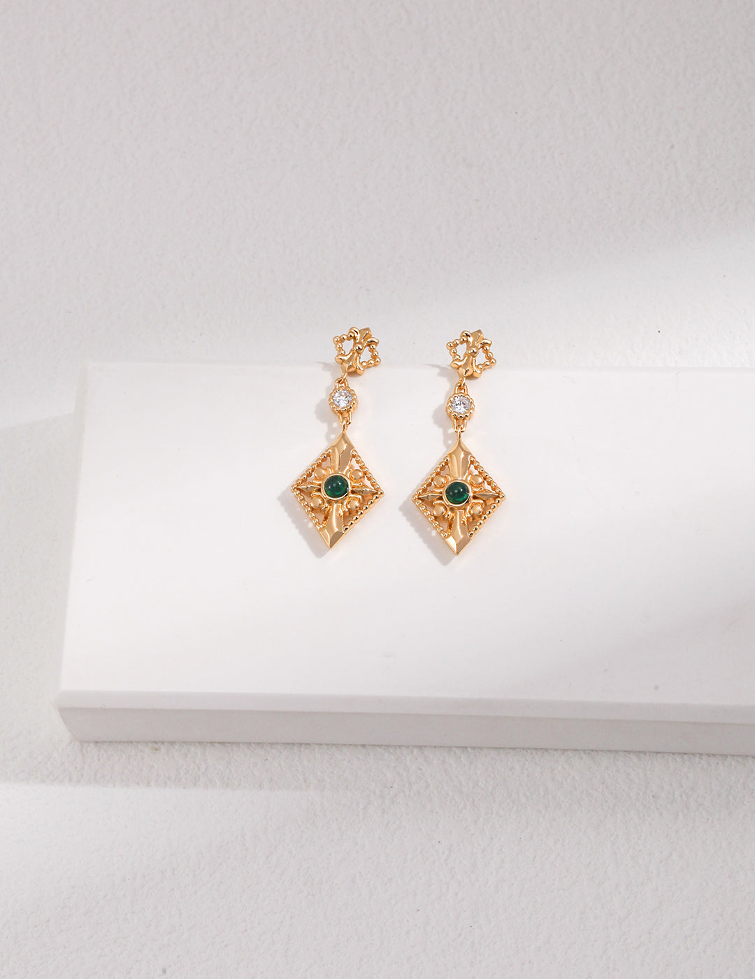 Gold earrings with green gemstones on a white surface