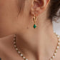A model wearing avant-garde drop earrings featuring organic sculptural 18k gold plated molten c-hoops suspending oval genuine green natural malachite stones