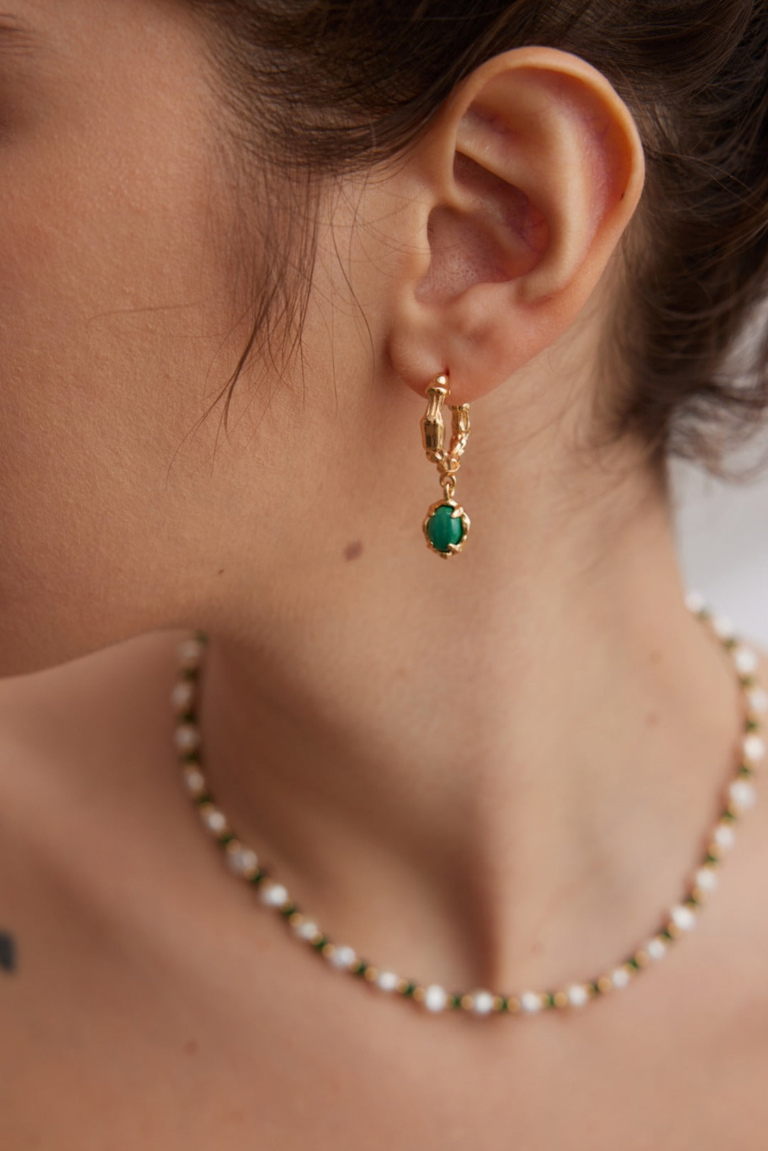 A model wearing avant-garde drop earrings featuring organic sculptural 18k gold plated molten c-hoops suspending oval genuine green natural malachite stones